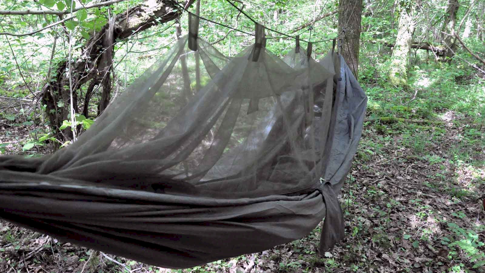 Image of the Snugpak Jungle Hammock pitched in woodland with the integrated mosquito net suspended above and a sleeping bag inside..