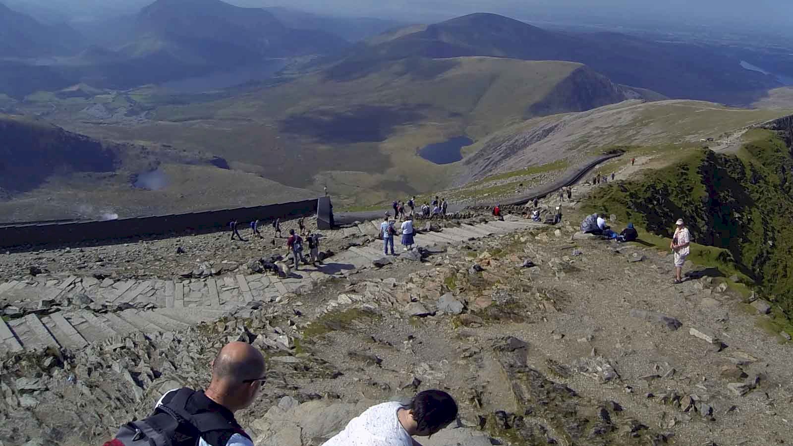 Picture of a comparatively quiet day on Snowdon summit mid summer. View from the summit trig point along the railway line into the valley.